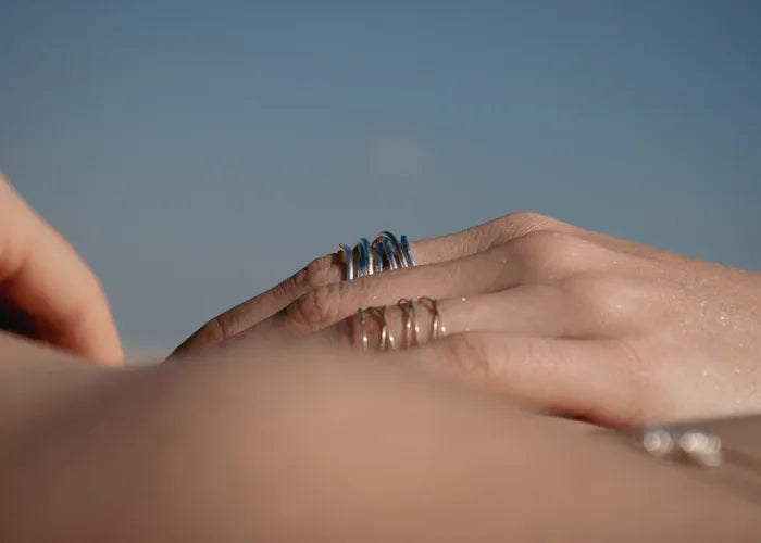 Zoom sur la main portant la bague Spirale LSonge en or et argent – fond ciel bleu