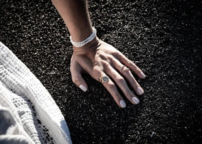 Main portant un bracelet Inara en perles blanches sur fond sombre