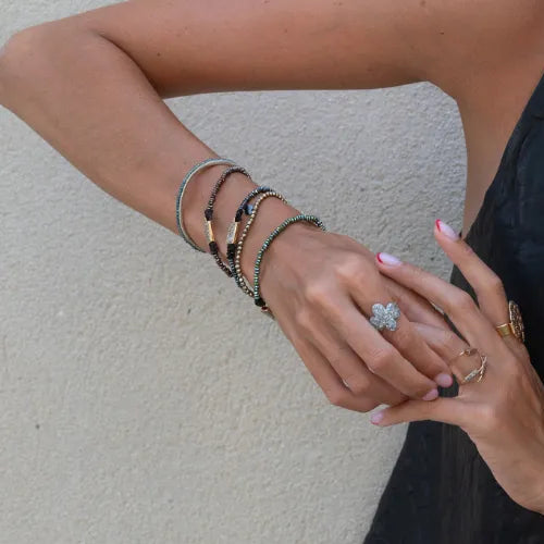 Gros plan sur des mains portant plusieurs bracelets One avec pierres et fermoirs dorés