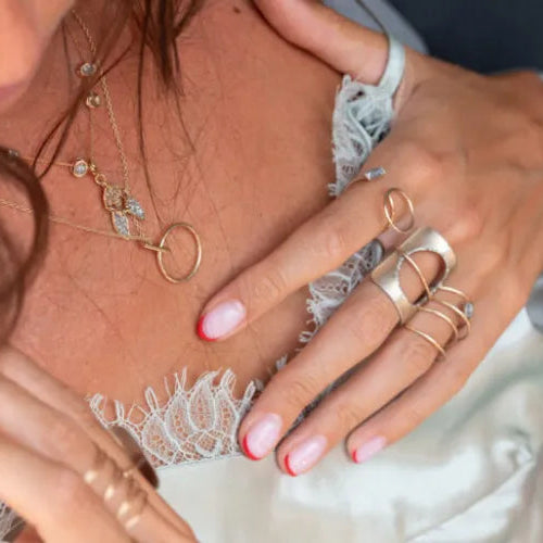 Gros plan sur des colliers fins portés sur un top en dentelle blanche.